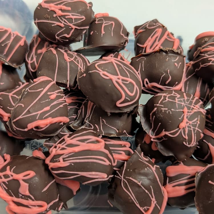 Heart shaped oreo truffles with a pink chocolate drizzle on top, sitting on a plate.